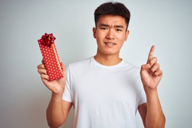 Sevgililer günü kartı tutan Asyalı genç adam izole edilmiş beyaz arka planda duruyor. Bir fikir ya da soru işareti ile şaşırmış, mutlu yüzle bir numara.