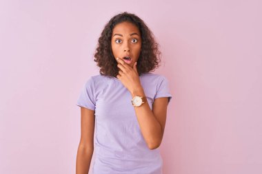 İzole edilmiş pembe arka plan üzerinde duran Brezilyalı genç bir kadın elleri çenesinde olan inançsızlıktan, şaşkınlıktan ve şaşkınlıktan büyülenmiş görünüyor.