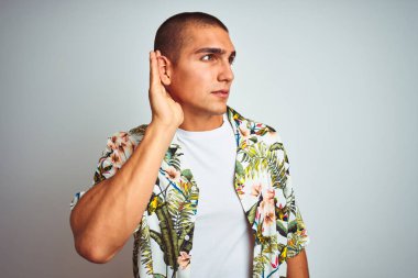 Tatilde, Hawaii gömleği giymiş, beyaz arka planda gülümseyen, kulağına fısıldayan ve dedikoduları dinleyen genç yakışıklı bir adam. Sağırlık kavramı.