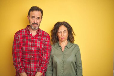 Güzel orta yaşlı çift, izole edilmiş sarı arka planda depresif ve endişeli, kızgın ve korkmuş bir şekilde ağlıyorlar. Üzücü ifade.