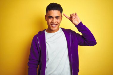Mor kazak giyen genç Brezilyalı adam izole edilmiş sarı arka planda duruyor. Tek parmakla kafasını göstererek gülümsüyor. Harika bir fikir ya da düşünce, iyi bir hafıza.
