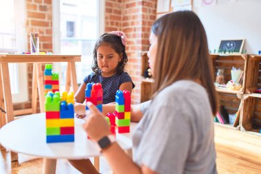 Güzel öğretmen ve küçük kız anaokulunda inşaat bloklarıyla oynuyorlar.