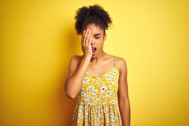 Siyah çiçekli bir elbise giyen Afro-Amerikalı kadın izole edilmiş sarı arka planda dikiliyor. Yarı yüz, göz ve ağzı elle kapatmaktan yoruluyor. Yüzüm acıyor..