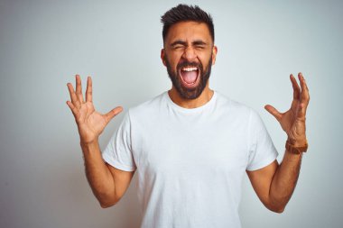 Young indian man wearing t-shirt standing over isolated white background celebrating mad and crazy for success with arms raised and closed eyes screaming excited. Winner concept