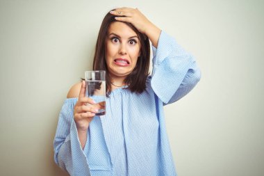 Genç ve güzel bir kadın, izole edilmiş arka planda bir bardak su içerken elleri başının üstünde, utanç ve şaşkınlık dolu, sinirli ve hayal kırıklığına uğramış bir halde. Hata için korku ve üzüntü.