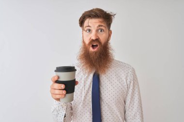 Genç kızıl saçlı adam kahveyi alıp götürüyor. İzole edilmiş beyaz arka planda duruyor. Şaşırmış bir yüz ifadesinden korkuyor ve heyecanlanıyor.