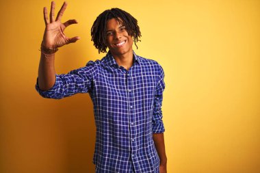 Rastgele tişörtlü Afro bir adam izole edilmiş sarı arka plan üzerinde duruyor gülümsüyor ve el hareketleriyle küçük boy işareti yapıyor parmakları bakıyor ve kameraya bakıyor. Ölçü kavramı.