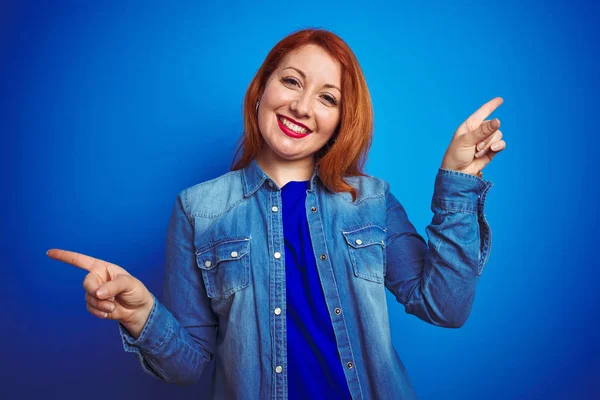 年轻美丽的红头发女人穿着斜纹棉布衬衫 站在蓝色孤立的背景上 带着自信的微笑 手指指向不同的方向 广告的复制空间 — 图库照片