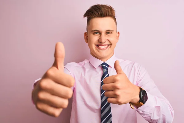 年轻英俊的商人穿着衬衫和领带站在孤立的粉红色背景批准做积极的姿态与手 竖起大拇指微笑和高兴的成功 获胜者手势 — 图库照片