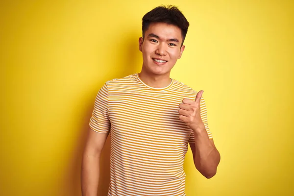 孤立した黄色の背景の上に立ってTシャツを着て若いアジア系中国人男性が手で幸せな親指をジェスチャーを行う 成功を示すカメラを見て表現を承認する — ストック写真
