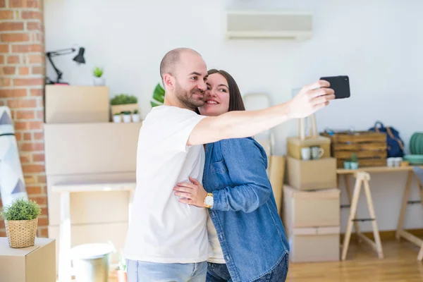 新居でスマホを使って写真を撮る若いカップル 新しいアパートに引っ越して嬉しそうに笑顔 — ストック写真
