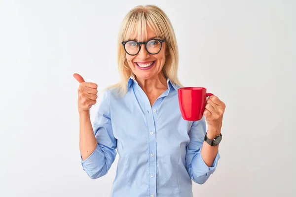 Middle age businesswoman wearing glasses drinking coffee over isolated white background happy with big smile doing ok sign, thumb up with fingers, excellent sign