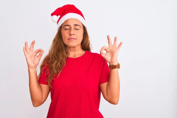 孤立した背景の上にクリスマスの帽子を身に着けている中年の成熟した女性は指で瞑想のジェスチャーをして閉じ目でリラックスして笑顔 ヨガのコンセプト — ストック写真