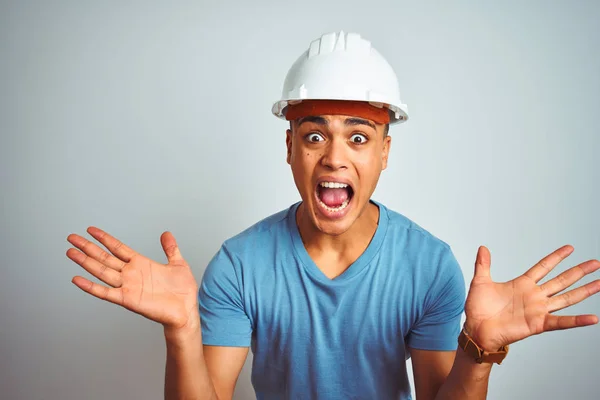 年轻的巴西工程师头戴安全帽 站在孤立的白色背景上庆祝疯狂和惊奇的成功 举起双臂 睁开眼睛兴奋地尖叫 赢的概念 — 图库照片