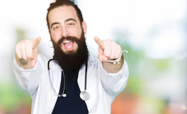 Доктор Довгим Волоссям Медичному Пальто Стетоскоп Вказуючи Камеру Пальцями Посміхаючись — стокове фото