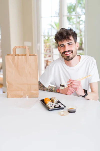 Young man eating sushi asian food and noodles using choopsticks