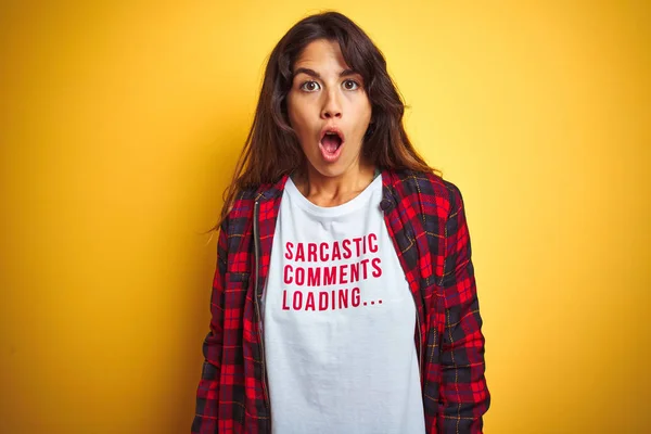 Beautiful woman wearing funny t-shirt with irony comments over isolated yellow background scared in shock with a surprise face, afraid and excited with fear expression