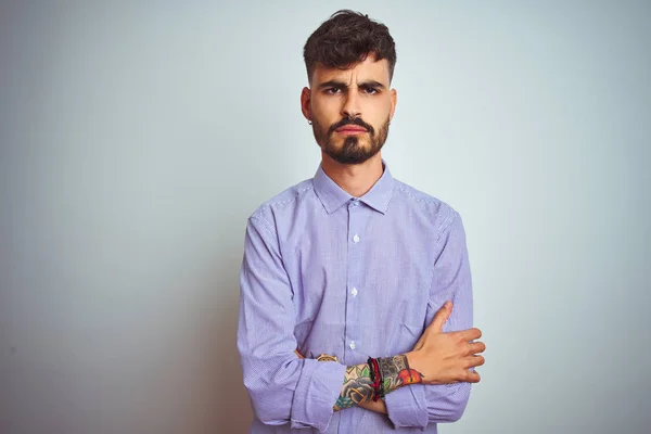 Young man with tattoo wearing purple shirt standing over isolated white background skeptic and nervous, disapproving expression on face with crossed arms. Negative person.