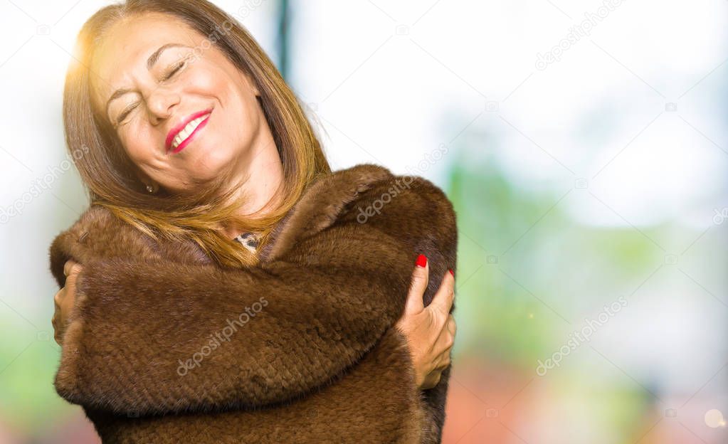 Beautiful middle age elegant woman wearing mink coat Hugging oneself happy and positive, smiling confident. Self love and self care