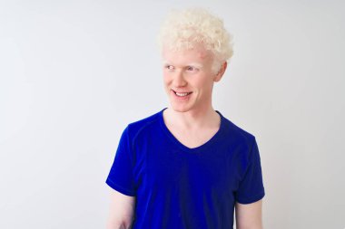 Mavi günlük tişört giyen genç albino adam izole edilmiş beyaz arka planda dikilip yüzünde gülümseme, doğal bir ifade ile yan yana bakıyor. Kendinden emin gülen.