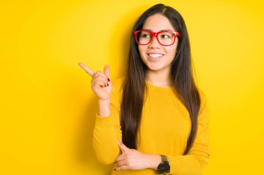 Güzel esmer kadın, sarı gözlüklü, izole edilmiş arka planda kırmızı gözlükler takıyor. Yüzünde kocaman bir gülümseme var. Eli ve parmağı kameraya bakıyor..