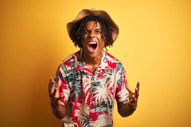 Rastalı gömlekli ve şapkalı Afro-Amerikan bir adam izole edilmiş sarı arka planda çılgın deli bağırıyor ve agresif bir ifade ve kolla bağırıyor. Hayal kırıklığı konsepti.