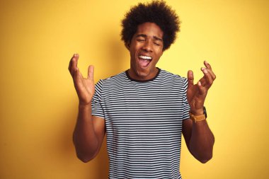 Afro saçlı Afro-Amerikalı adam izole edilmiş sarı arka plan üzerinde donanma çizgili tişört giyiyor ve kollarını kaldırmış ve gözleri kapalı bir şekilde heyecanla haykırarak başarının çılgınlığını kutluyor. Kazanan konsept