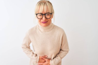 Orta yaşlı kadın balıkçı yaka kazak ve gözlük takıyor. İzole edilmiş beyaz arka planda, midesi üstünde. Çünkü hazımsızlık, acı veren hastalıklar, kendini iyi hissetmiyor. Ache kavramı.