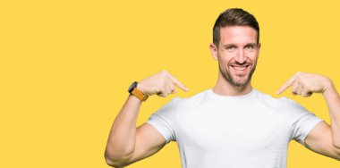 Yakışıklı adam yüzünde gülümseme ile kendinden emin görünüyorsun, kendini gururlu ve mutlu parmakları ile işaret casual beyaz t-shirt giyen.