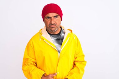 Yağmurluk giyen ve yünlü şapka takan orta yaşlı bir adam izole edilmiş beyaz arka plan kuşkucu ve gergin duruyor, sorun yüzünden suratını asıyor. Negatif kişi.