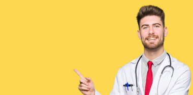 Yüzünde büyük bir gülümseme ile tıbbi ceket giyen genç yakışıklı Doktor adam, kamera bakarak yan el ve parmak ile işaret.