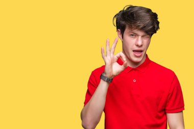 Seksi bir ifadeyle, neşeli ve mutlu yüzünü kameraya bakarak göz kırpıyor izole arka plan üzerinde kırmızı t-shirt giyen genç yakışıklı adam.