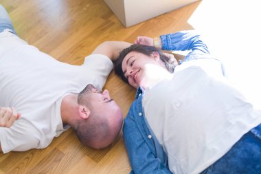 Yeni bir evin katında yatan aşık genç çift, yeni bir daireye taşınmak için çok mutlu gülümseyen, karton kutular civarı