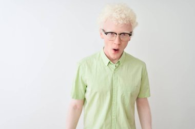 Yeşil tişört ve gözlük takan genç sarışın adam beyaz arka plan üzerinde korkmuş ve şaşırmış bir ifade, korku ve heyecan dolu bir yüz..