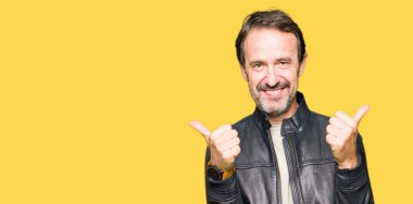 Siyah deri ceket başarı işareti giyen orta yaş yakışıklı adam el ile olumlu jest yapıyor, gülümseyen ve mutlu kadar başparmak. Neşeli ifade ile kamera bakarak, kazanan jest.