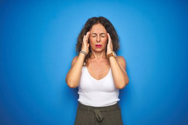 Orta yaşlı, kıvırcık saçlı, mavi izole edilmiş arka planda duran, stresten dolayı baş ağrısı çeken bir kadın. Migren ağrısı..