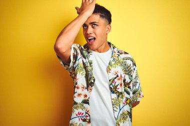 Tatilde olan genç Brezilyalı bir adam yaz çiçekli gömleğini giyip izole edilmiş sarı arka planda hata sonucu el ele tutuşarak şaşırmış. Hatayı hatırla. Unuttum, kötü hafıza konsepti.