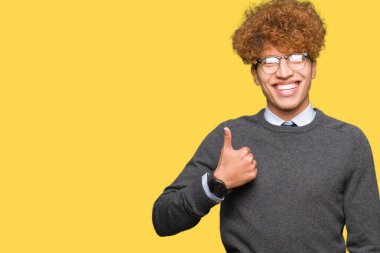 Afro saçlı genç yakışıklı iş adamı gözlük takıyor mutlu başparmaklar el ile jest yapıyor. Başarı göstererek kameraya bakan ifadeyi onaylama.