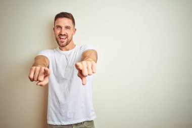 Casual beyaz t-shirt üzerinde izole giyen genç yakışıklı adam arka plan size işaret ve parmaklar, kamerayla olumlu ve neşeli gülümseyen