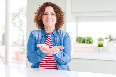 Kıvırcık saçlı, kot ceket giyen, elleri avuçlarında gülümseyen, el hareketi yapan orta yaşlı bir kadın. Tutun ve koruyun