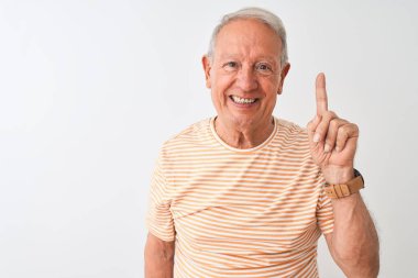 Kıdemli gri saçlı, çizgili tişört giyen, izole edilmiş beyaz arka planda duran ve bir numarayı işaret eden, kendinden emin ve mutlu gülümseyen adam..