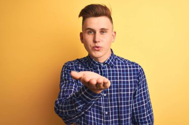 Sarı arka plan üzerinde duran rahat tişörtlü genç yakışıklı bir adam havayla öpüşürken kameraya bakıyor. Güzel ve seksi. Aşk ifadesi.