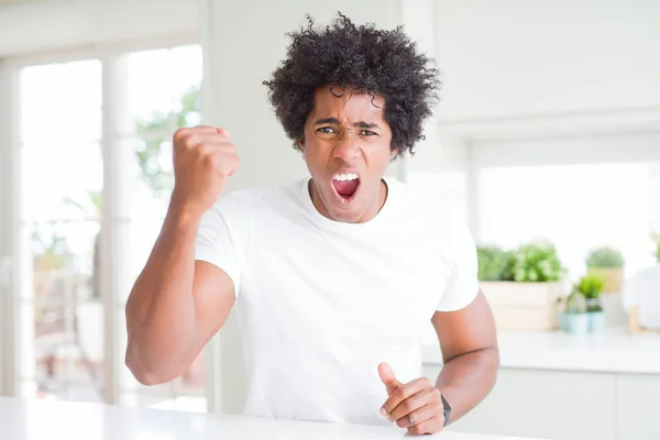 若いアフリカ系アメリカ人の男性は 怒って怒って家に座っているカジュアルな白いTシャツを着て 怒りを叫びながら拳をフラストレーションと激怒を上げています 激怒と積極的な概念 — ストック写真