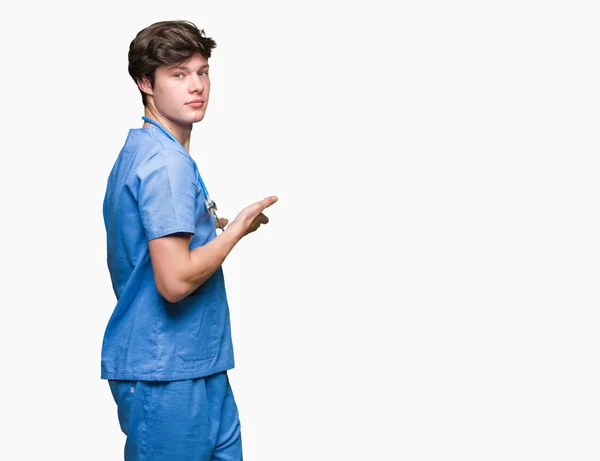 年轻的医生穿着医疗制服在孤立的背景邀请进入微笑自然与开放的手 — 图库照片
