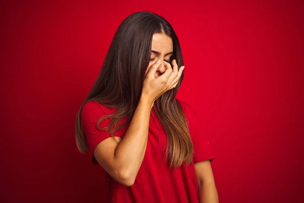 若い美しい女性のTシャツを着て孤立した赤い背景に立って疲れ鼻と目の疲れや頭痛を感じる摩擦疲れて立っている ストレスとフラストレーションの概念 — ストック写真