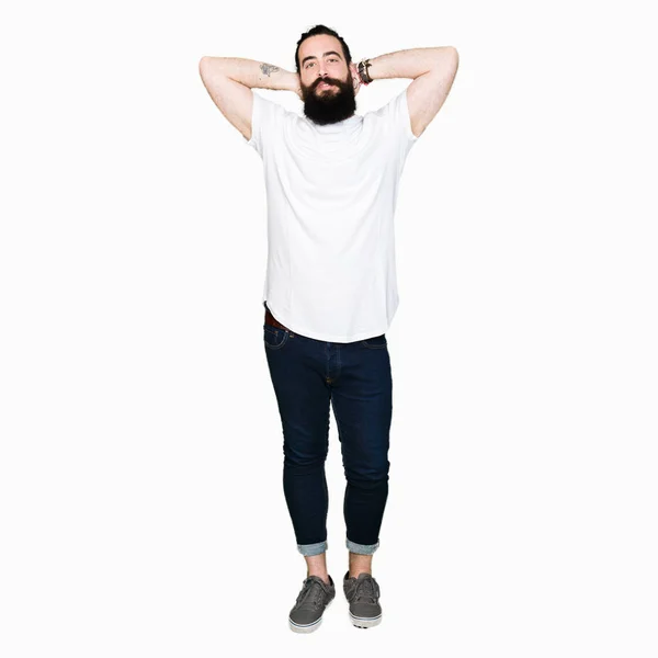 年轻的时髦男子长头发和胡须穿着休闲的白色T恤放松和伸展与手臂和手后头和脖子 微笑快乐 — 图库照片