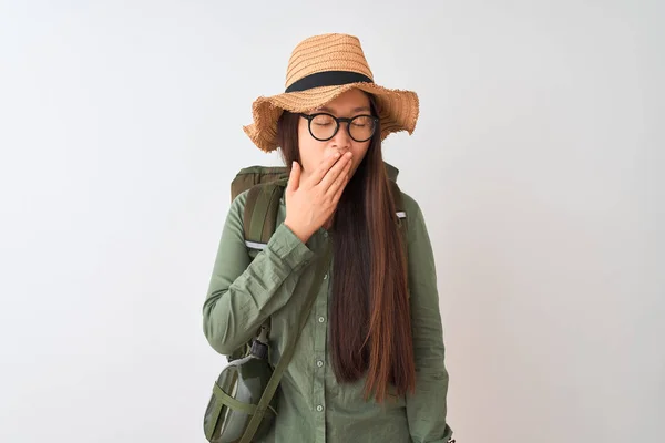 Chinese hiker woman wearing canteen hat glasses backpack over isolated white background bored yawning tired covering mouth with hand. Restless and sleepiness.