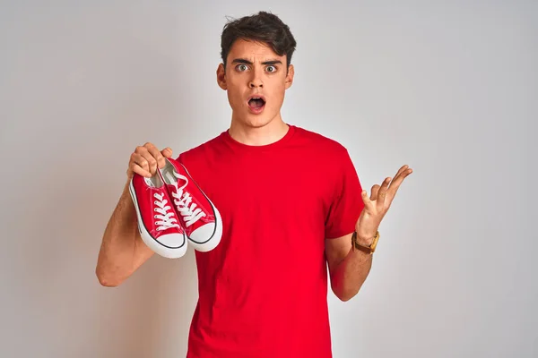 Tonårspojken Håller Mode Och Casual Sneakers Över Röd Isolerad Bakgrund — Stockfoto