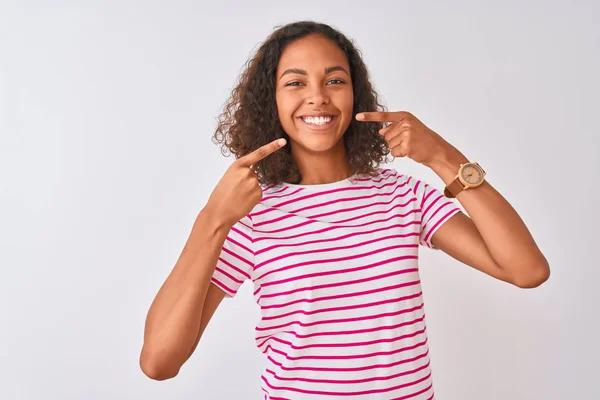 ピンクの縞模様のTシャツを着た若いブラジル人女性は 明るい表情と指の歯と口で指して笑顔で孤立した白い背景の上に立っています 歯科衛生の概念 — ストック写真