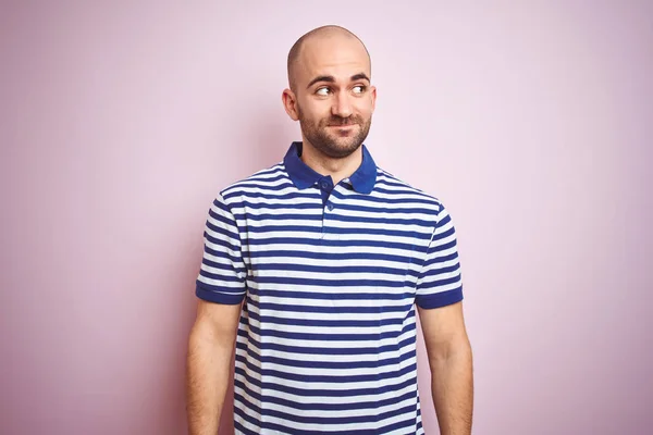 Young bald man with beard wearing casual striped blue t-shirt over pink isolated background smiling looking to the side and staring away thinking.
